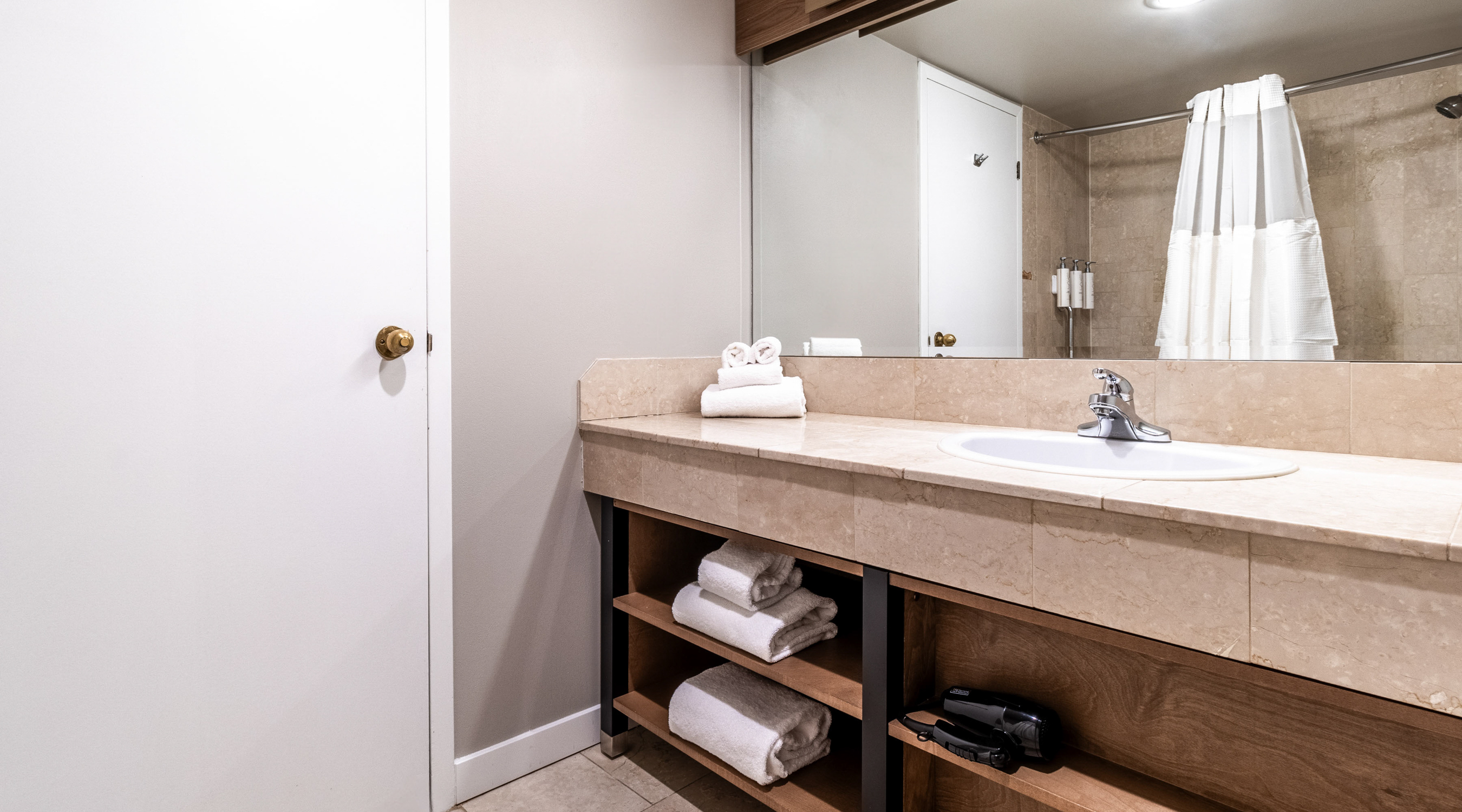 Guest room bathroom with vanity, sink, mirror, open towel shelving, and walk-in shower for a comfortable stay.