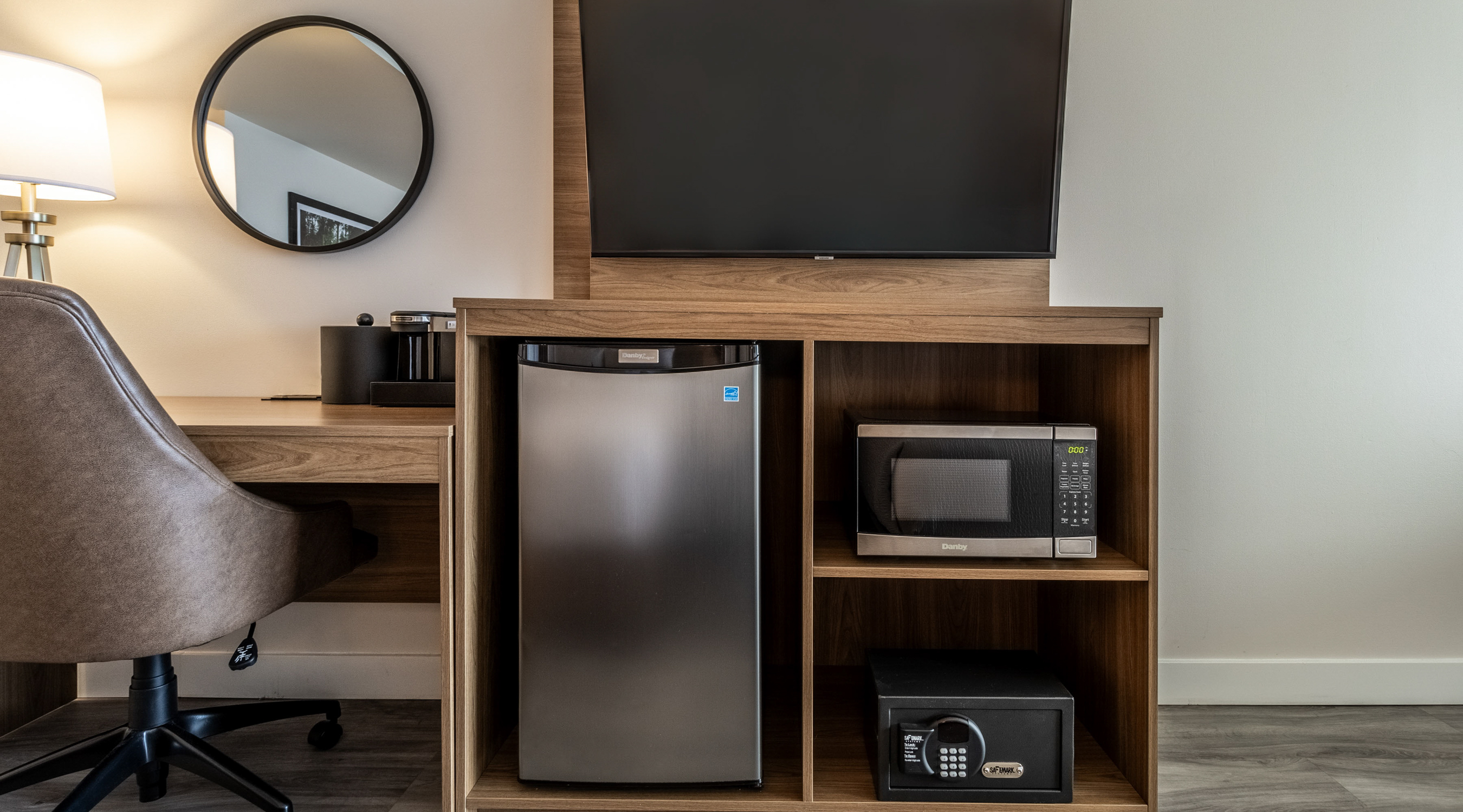 Guest room work area with desk, mini fridge, microwave, in-room safe, and flat-screen TV for a comfortable stay.
